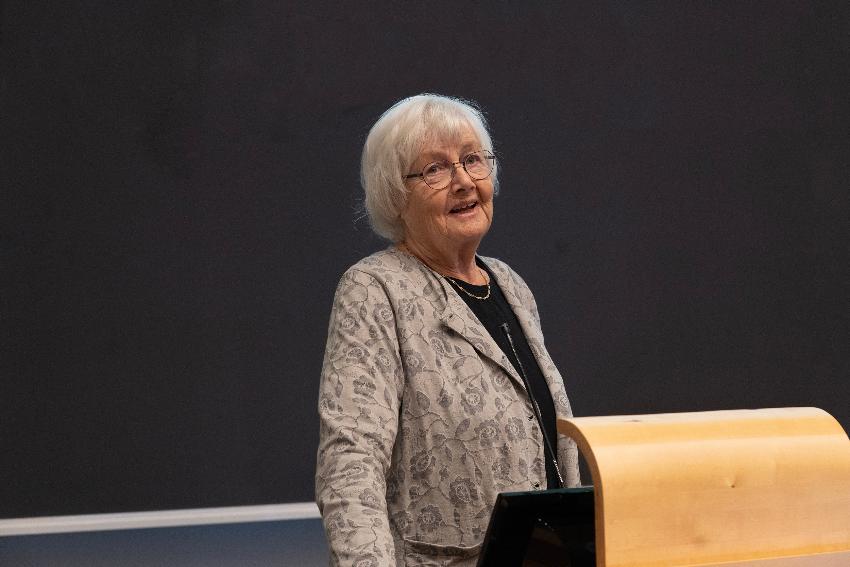 Kvinne taler til et publikum, som ikke er i bildet. 