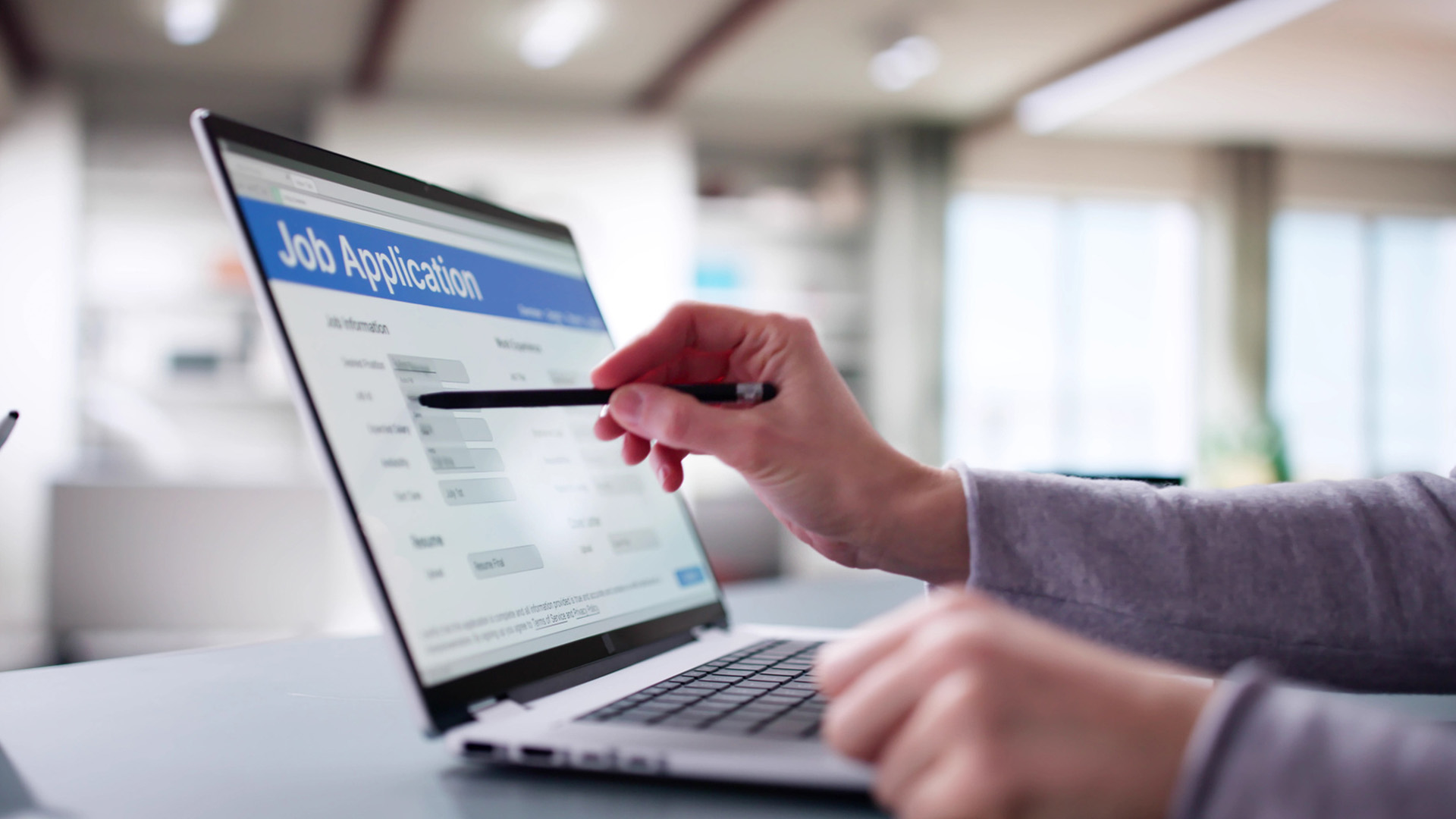 A photo of an arm pointing to a computer screen with a job application on-screen