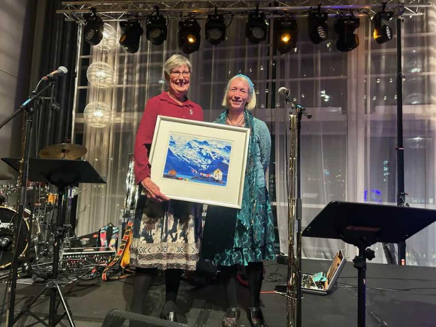 To kvinner på en scene, hvor den ene kvinnen skal overlevere et bilde til prisvinneren.