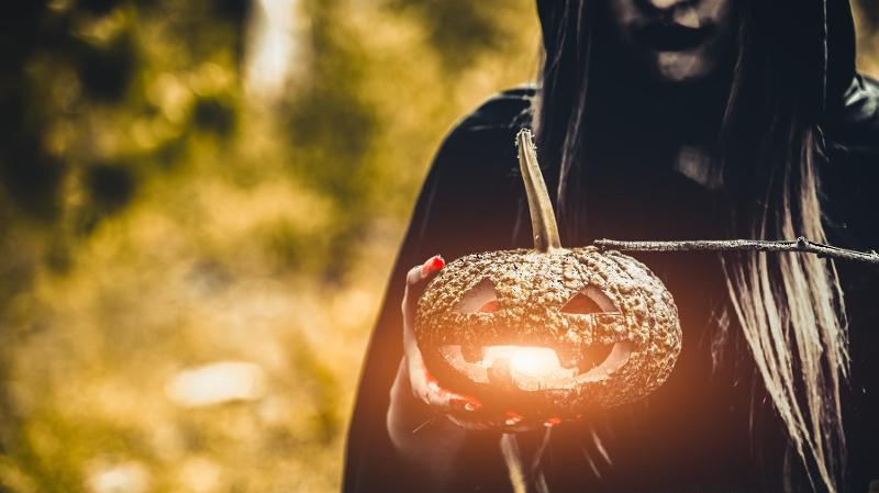 dame med mørk kappe som holder gresskarlykt