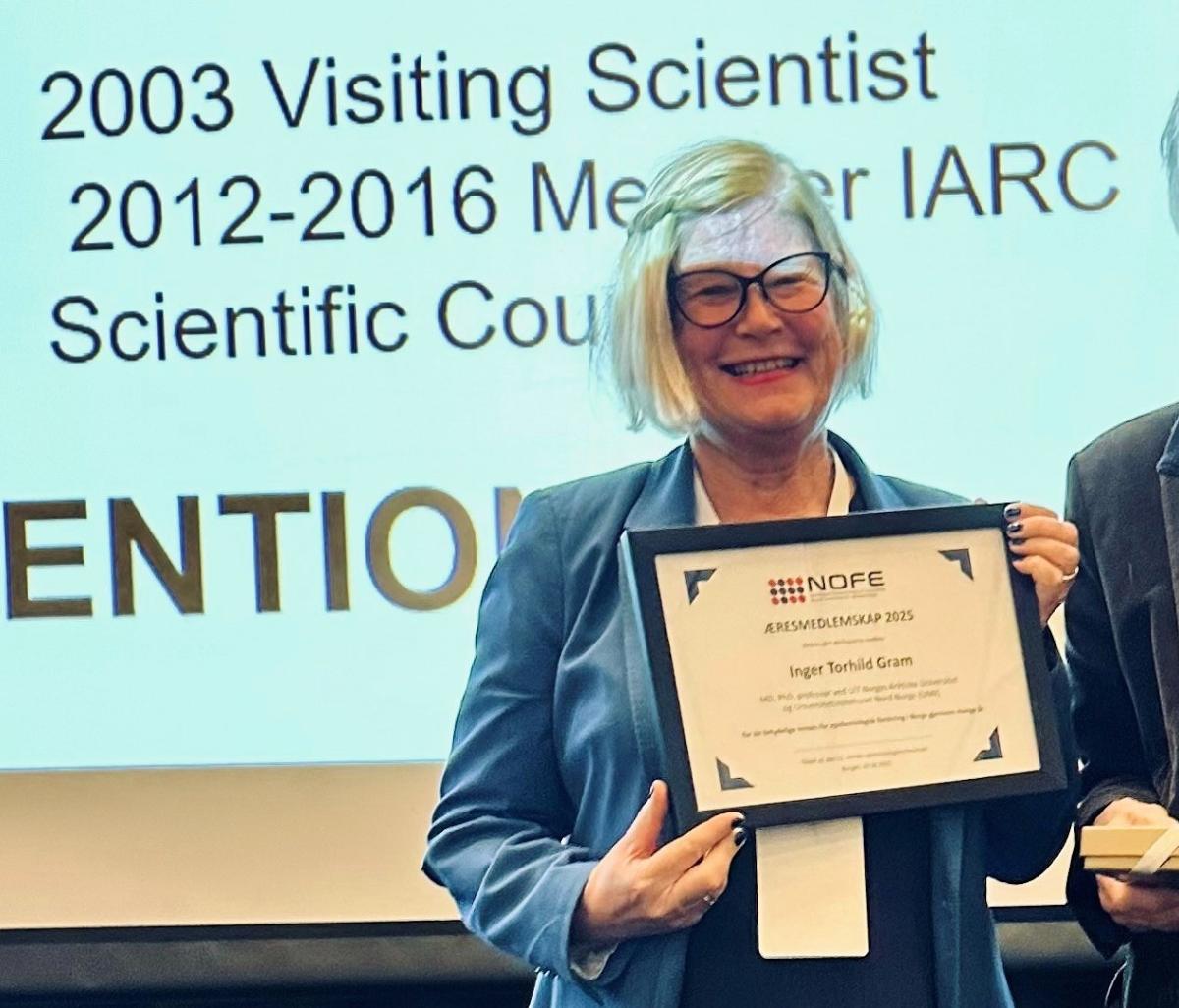 Kvinne med diplom. Hun smiler stort. 