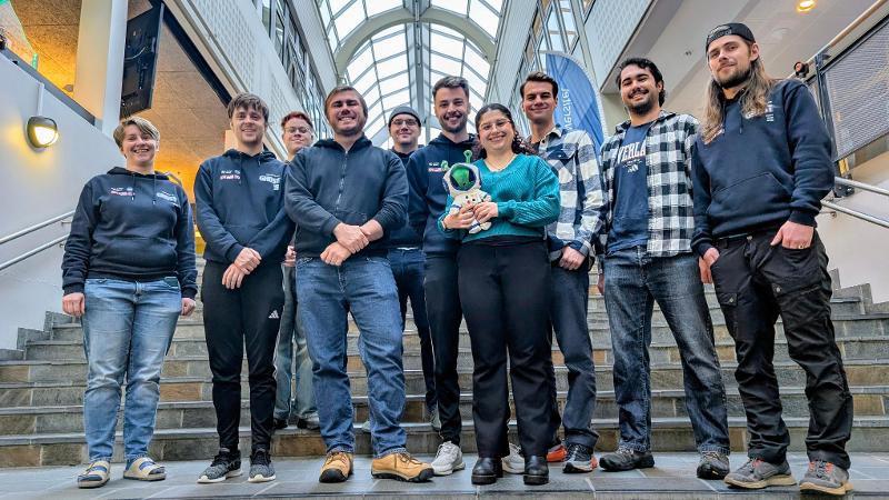 mange studenter som står på rekke og rad med stor glass hall bak 