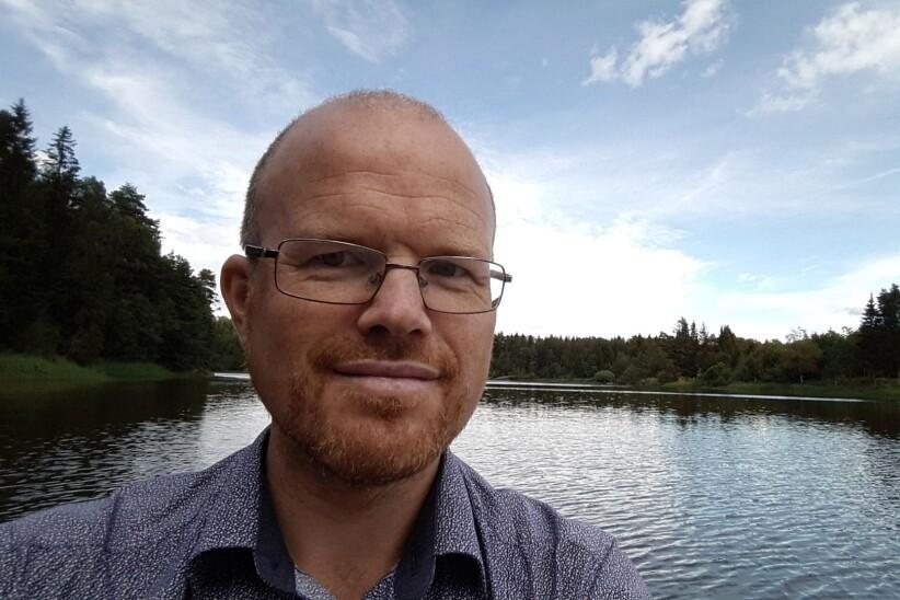 Ansiktet til en mann som står ved en innsjø, omgitt av skog