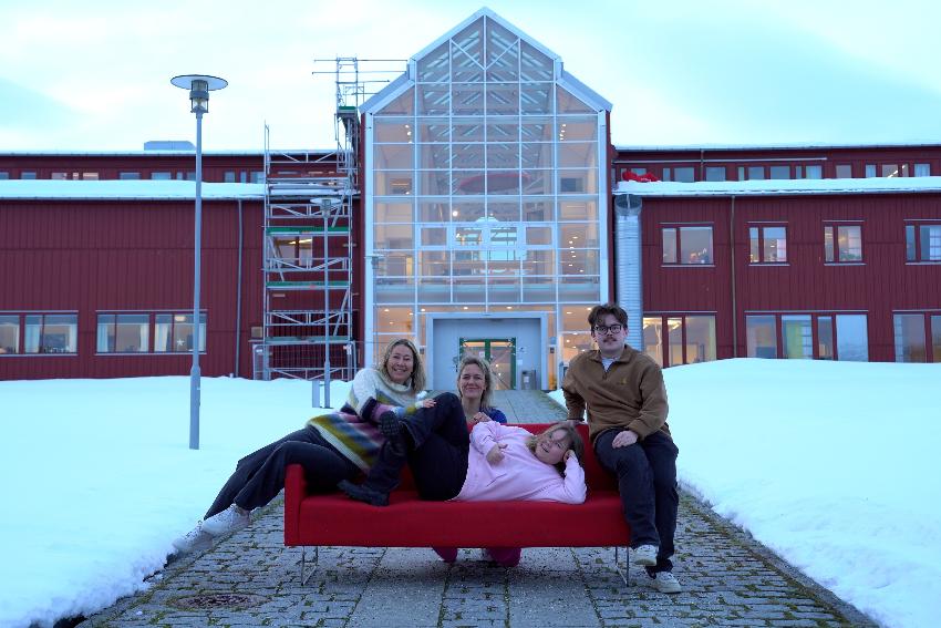 Fire personer som sitter i en sofa, utenfor inngang til et bygg, i et vinterlandskap.