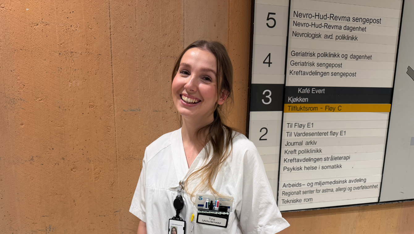 Kvinne i sykehusuniform foran vegg. 