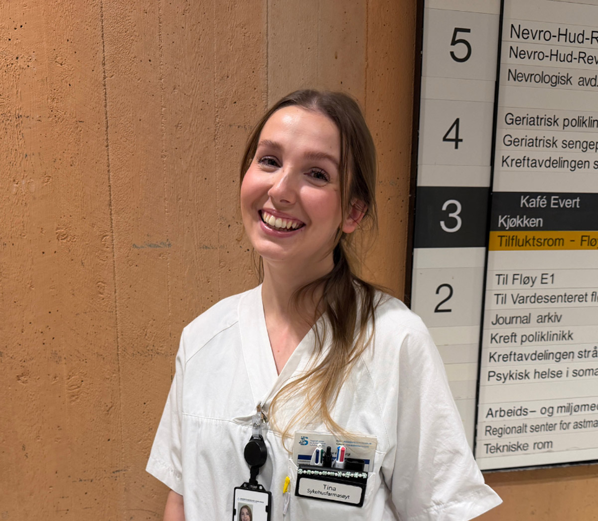 Kvinne i sykehusuniform foran vegg. 