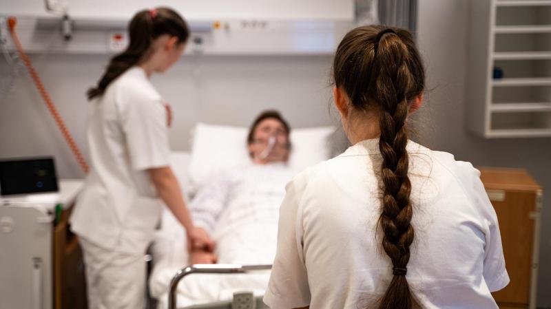 to mennesker med sykepleieuniform som står ved en seng med en pasient