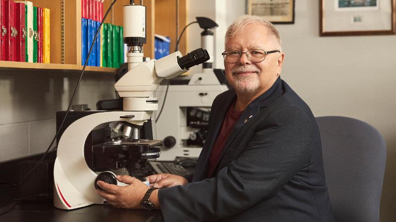 Ein smilande mann ved eit mikroskop på ein lab