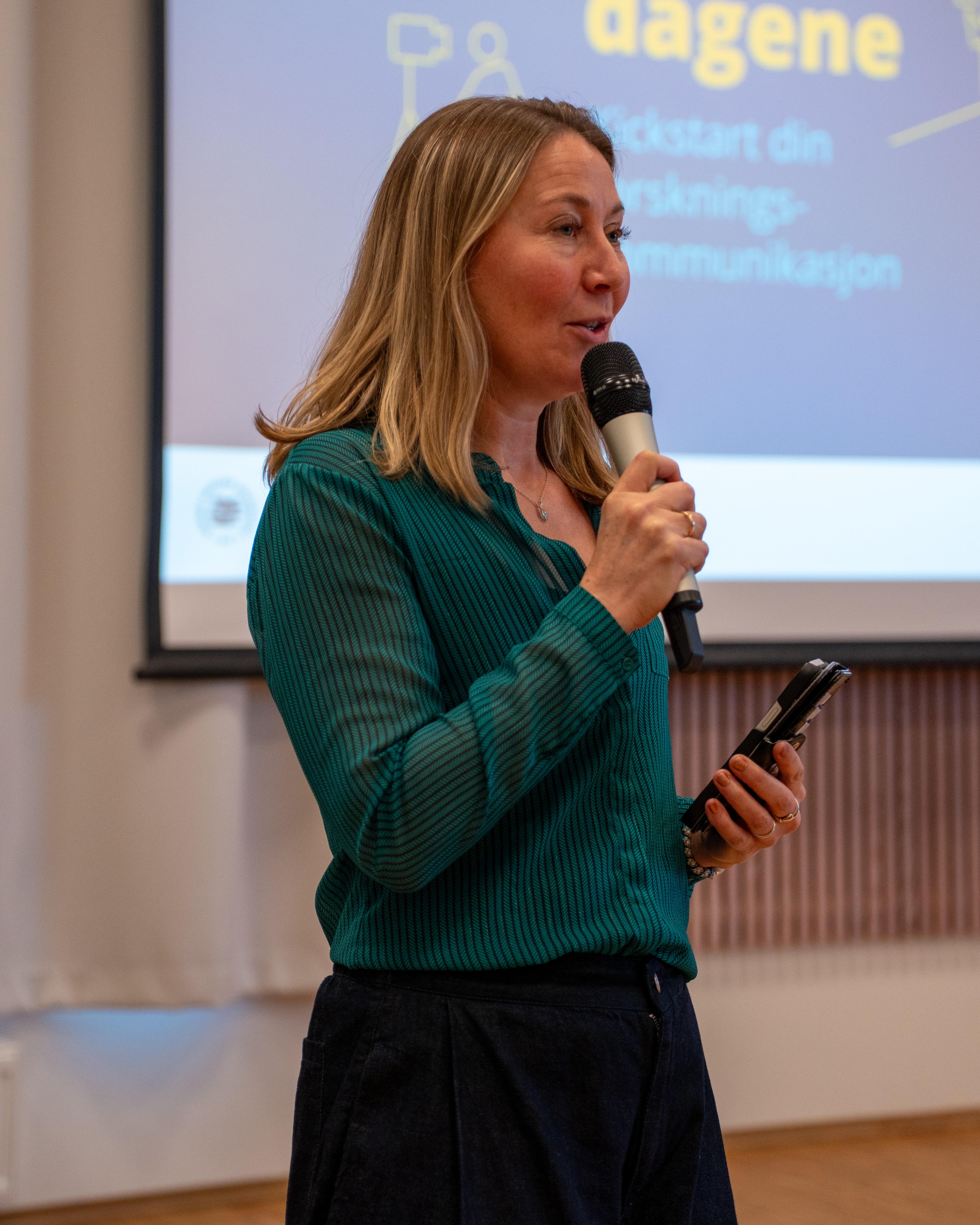 Kvinne som holder en mikrofon, med en storskjerm i bakgrunnen.