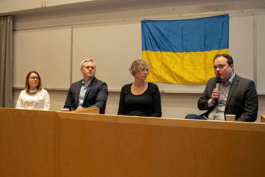 Fire personer som sitter p&aring; linje rundt et bord.