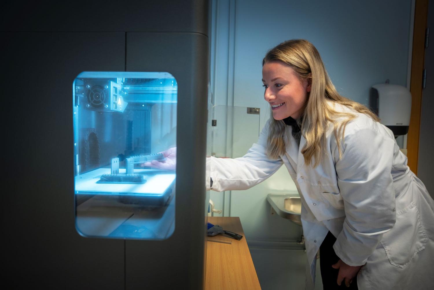 PhD kandidat i hvit laboratoriefrakk som holder en 3D-modell av deler hun studerer