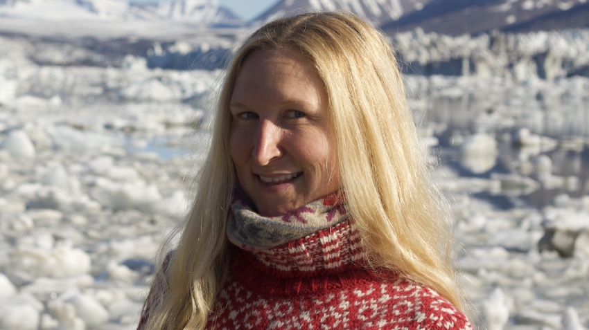 Portrettbilde av lyshåret kvinne i rød ullgenser i arktisk landskap