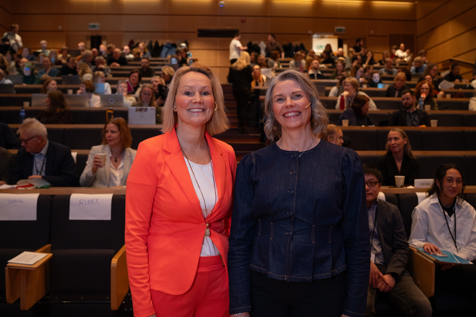 To kvinner foran publikum i et universitetsauditorium.