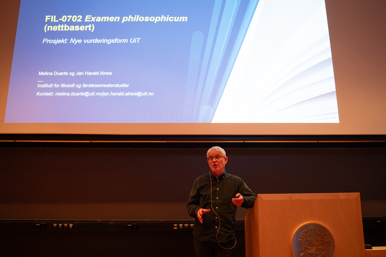 Mann holder innlegg foran stor powerpoint-oppslag. 