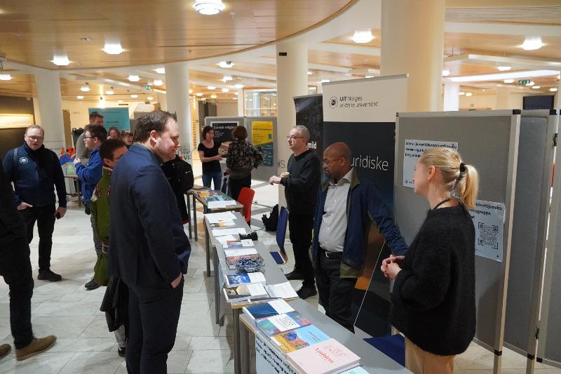 Mann med m&oslash;rkt h&aring;r m&oslash;tter to mennesker ved et stand