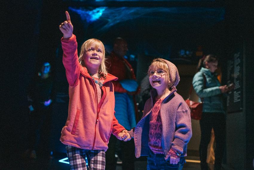 To barn peker og og smiler og ser på noe i taket