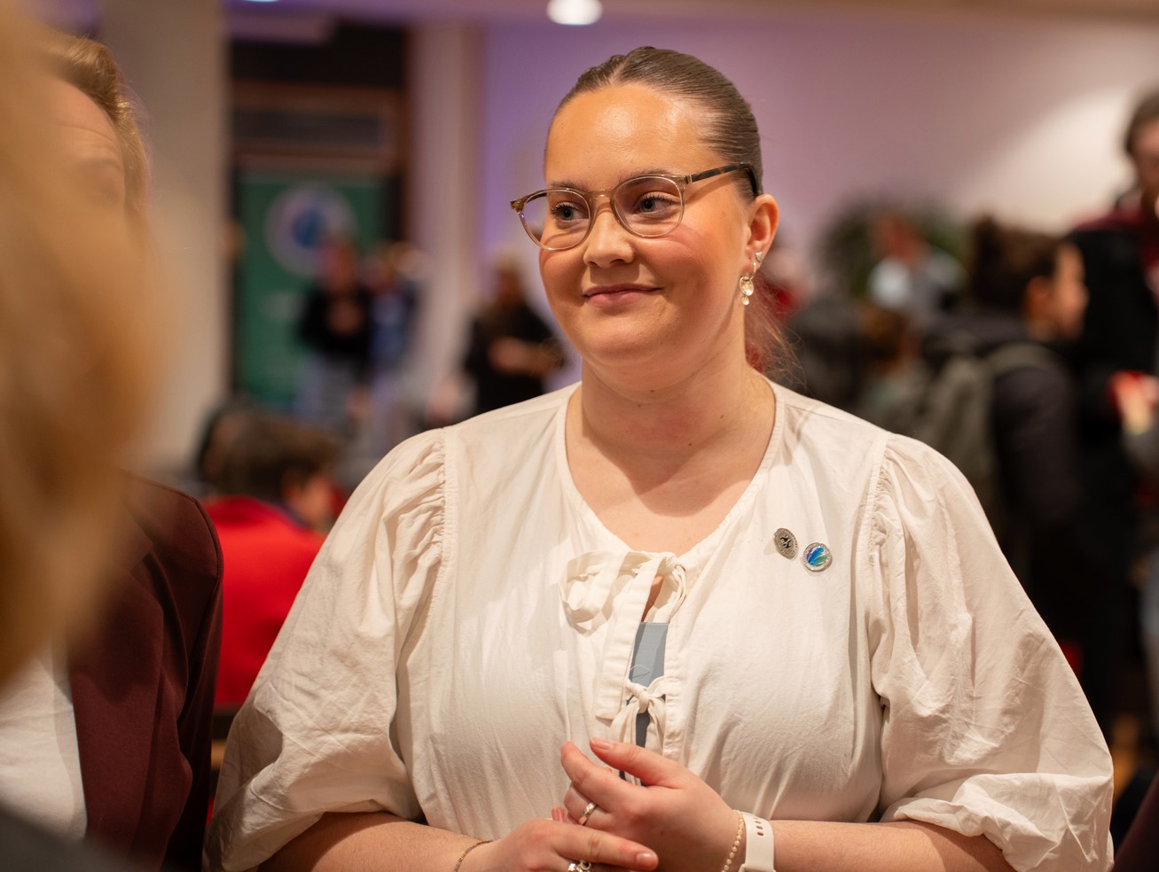 Kvinne med briller i samtale med en rekke andre folk. 