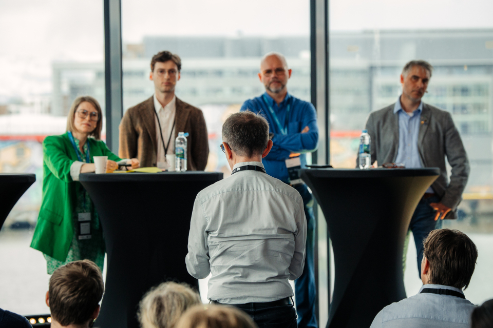 mennesker som st&aring;r p&aring; en scene mens en annen st&aring;r i publikum og stiller et sp&oslash;rsm&aring;l