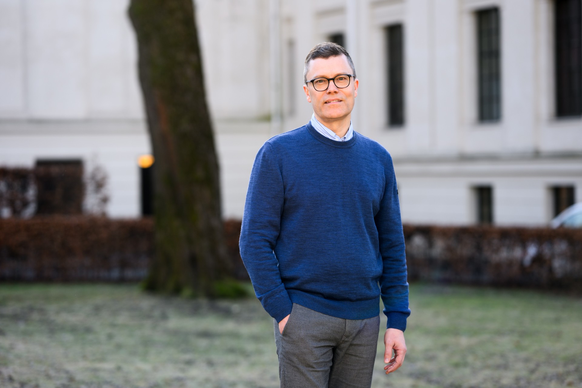 Mann, briller, kort h&aring;r, bl&aring; genser, poserer ute, ser i kamera