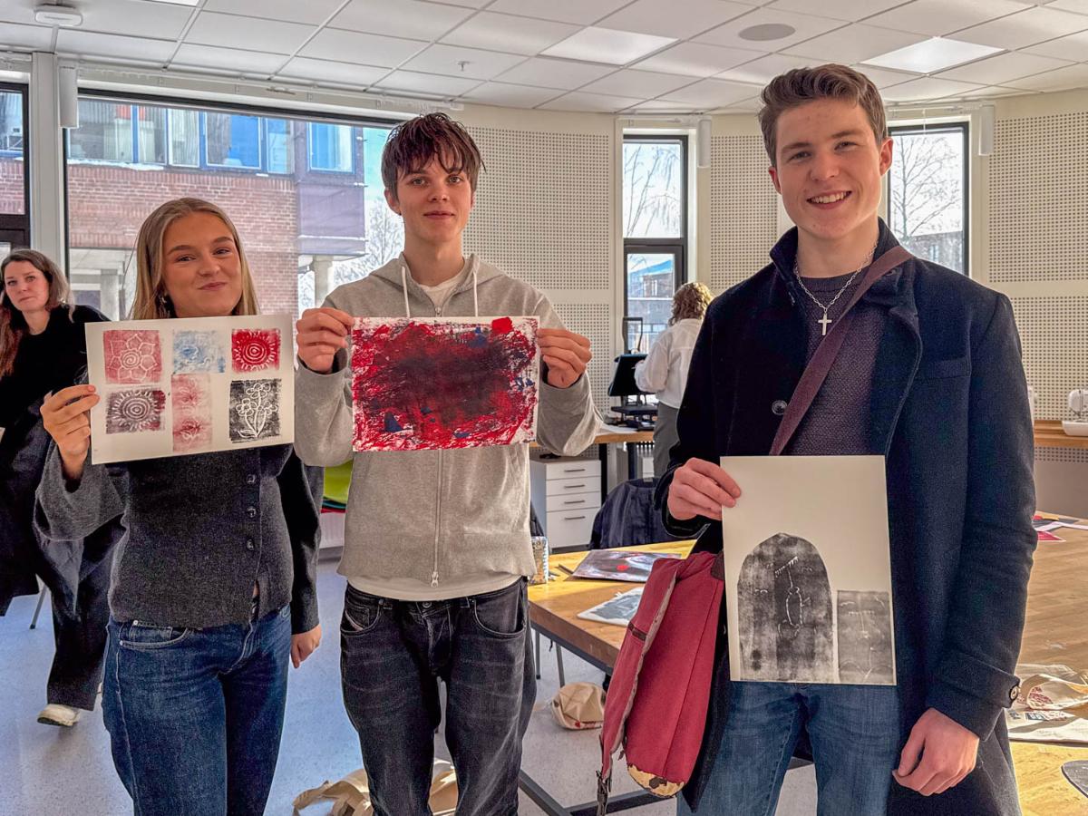En jente og to gutter fra videreg&aring;ende skole viser fram fargerike trykk de har laget selv. 