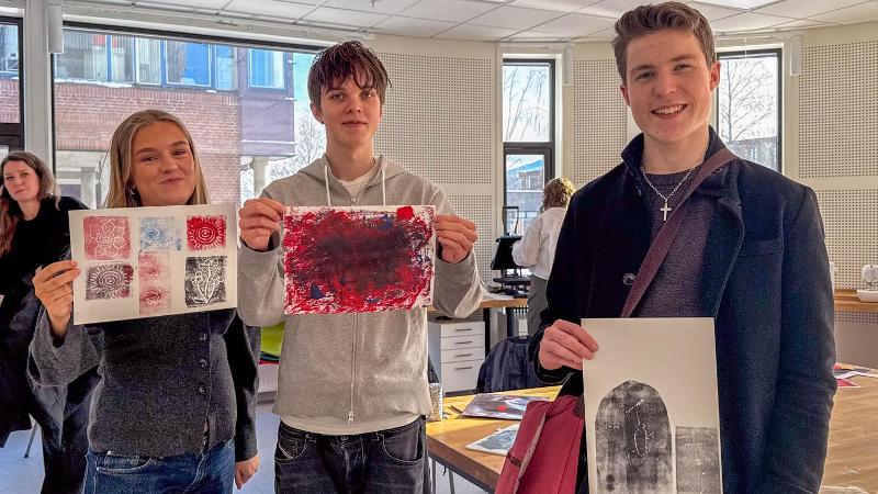 tre ungdommer som holder opp tre tegninger og smiler