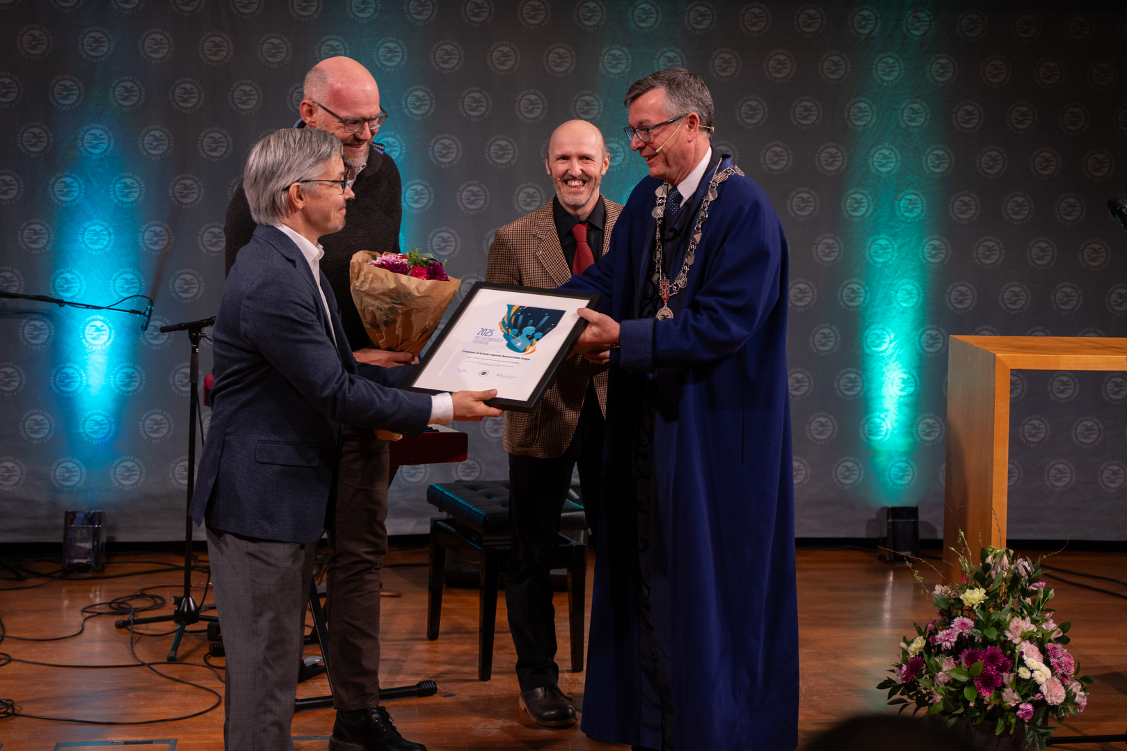 Tre mottar diplom, blomster og gave av universitetsrektor. 