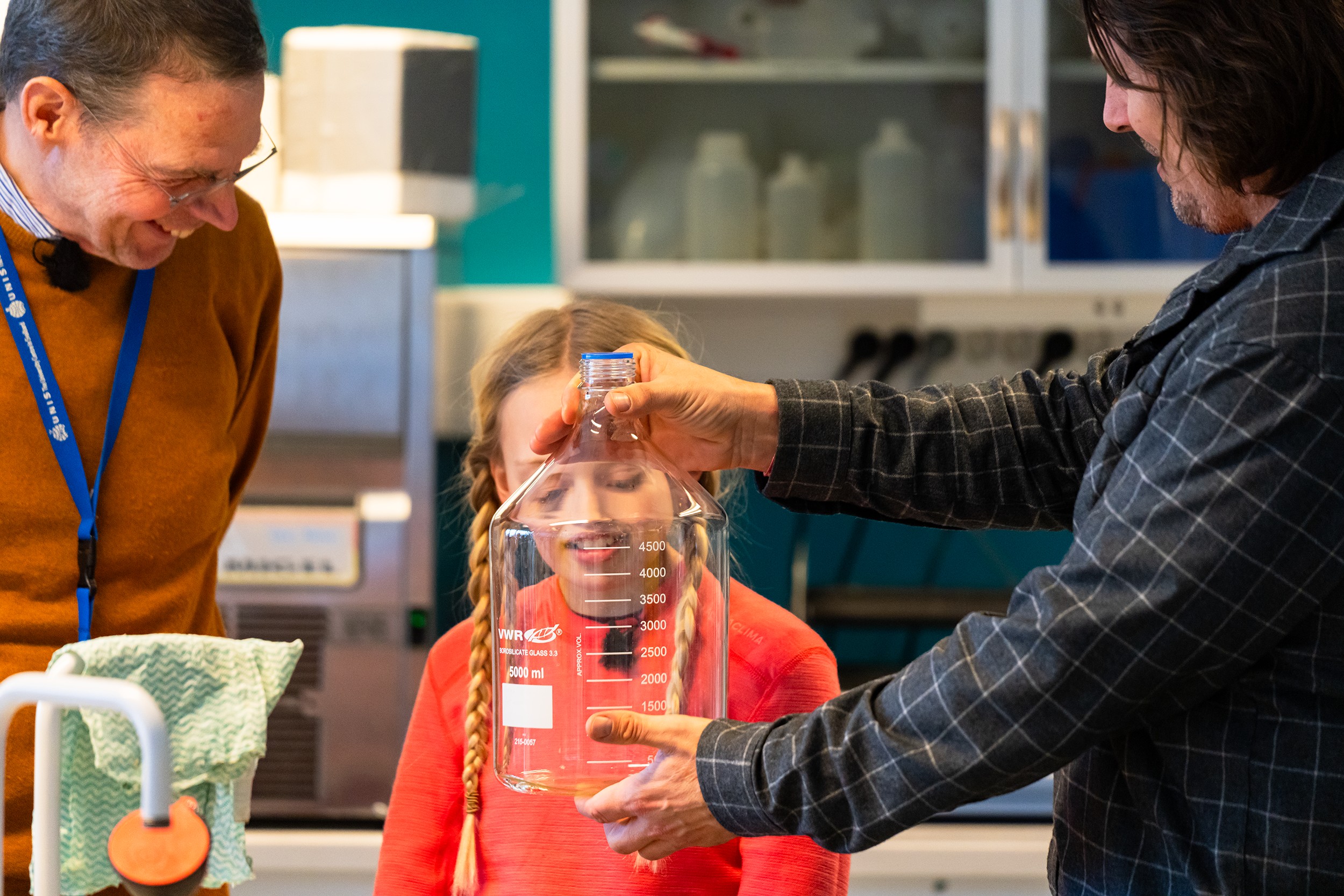 jente som ser p&aring; en stor flaske med to menn som st&aring;r ved siden av