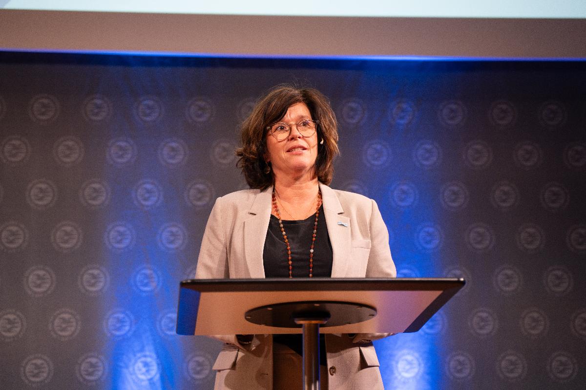 kvinne, kort, brunt h&aring;r, briller, snakker i mikrofon. 