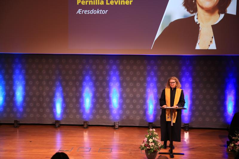 kvinne, har p&aring; kappe med gult b&aring;nd over skuldrene