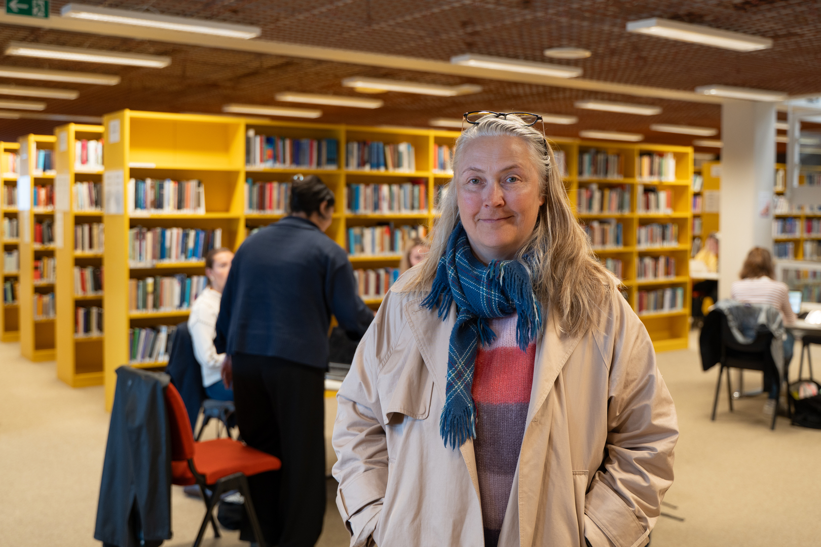 Kvinne st&aring;r midt i et folksomt bibliotek 