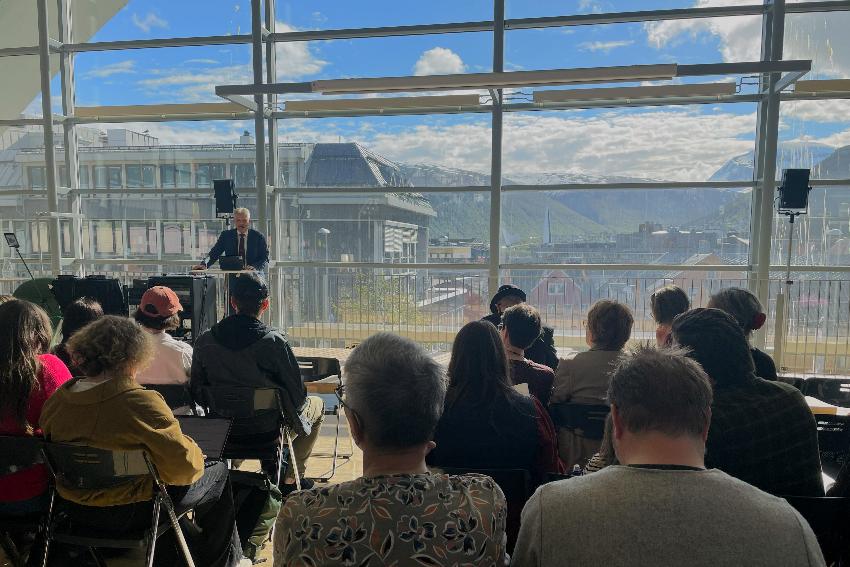 ein mann snakkar for eit publikum bak han ein glasvegg med utsikt til Troms&oslash;