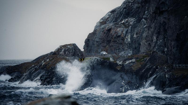 b&oslash;lge som sl&aring;r inn mot land der bil kj&oslash;rer p&aring; en kronglete vei