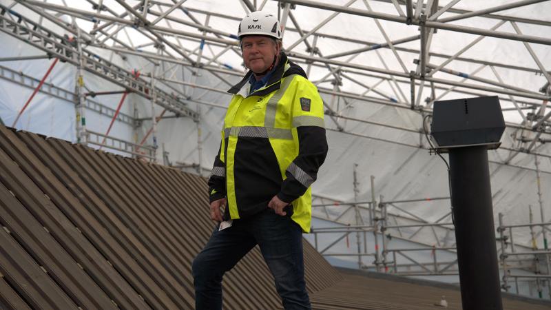 mann som st&aring;r med byggekl&aelig;r opp&aring; et tak