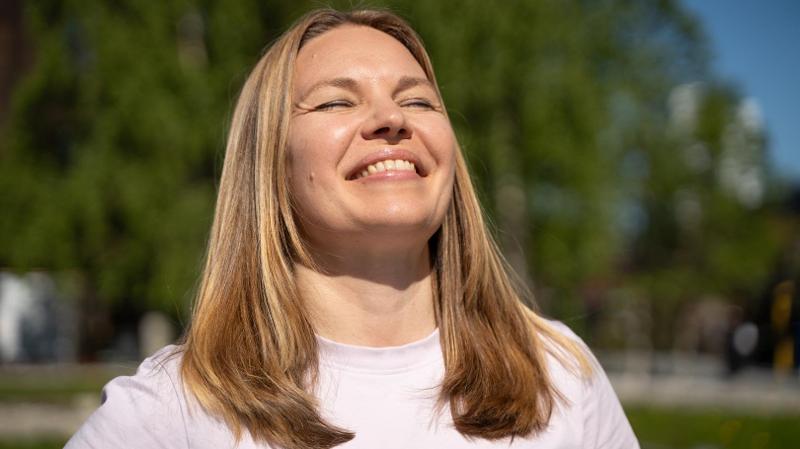 dame som st&aring;r med ansiktet mot sola med &oslash;ynene lukket