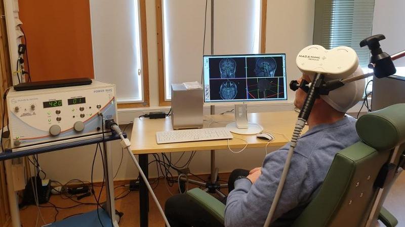 en person med medisins apparat p&aring; hodet sitter ved en dataskjerm