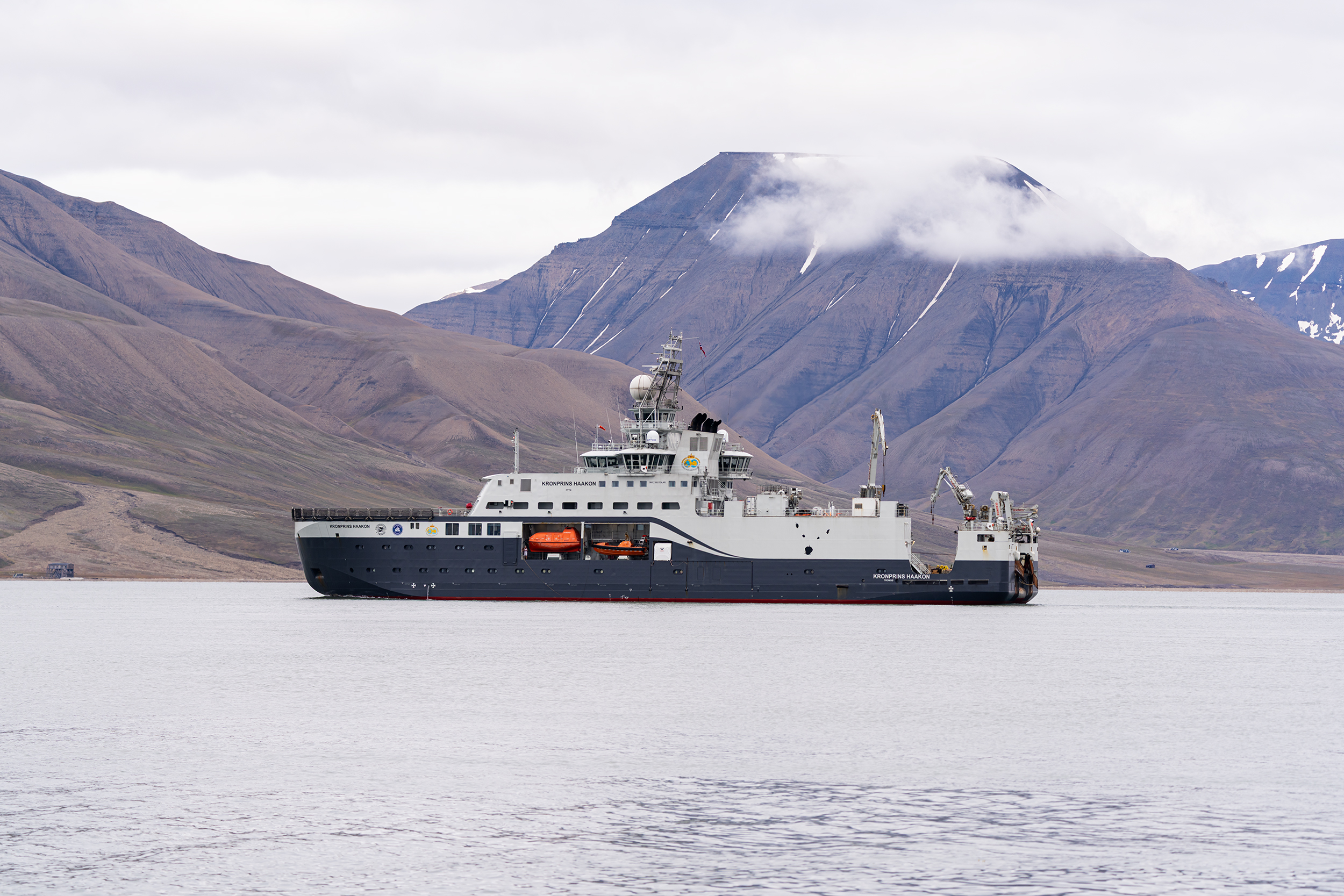 Skip ved kysten av Svalbard, med fjell bak.