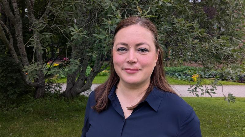 dame med m&oslash;rkt h&aring;r som st&aring;r foran tr&aelig;r