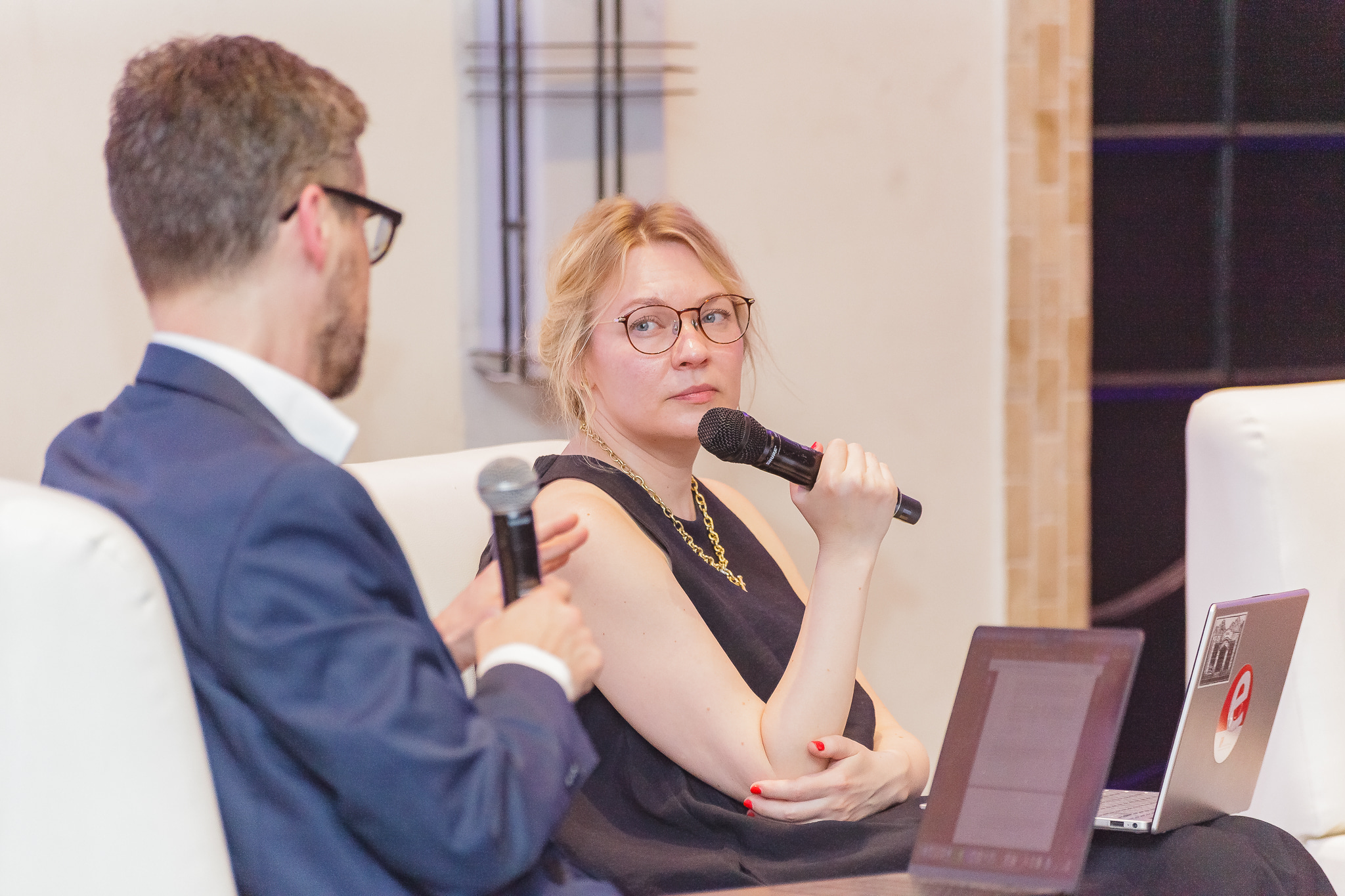 woman talking in microphone, blond hair, wearing glasses