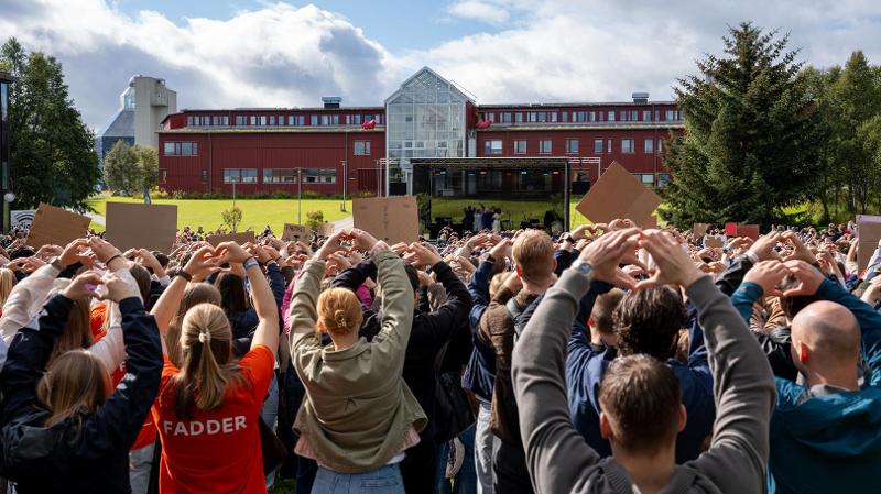 mange mennesker som st&aring;r samlet ute og holderhjerteform med hendene