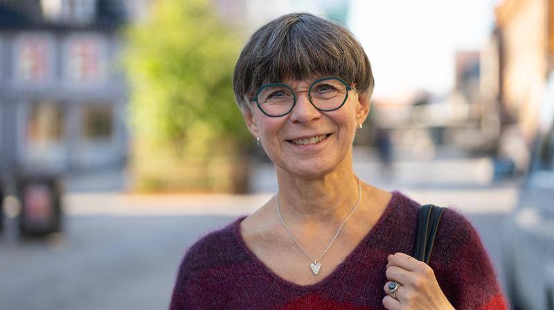 dame med kort h&aring;r og briller som st&aring;r ute foran universitetsbygg