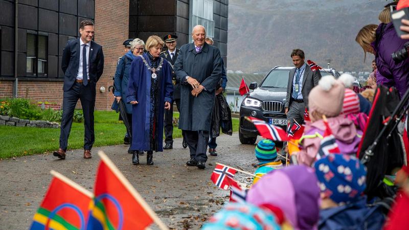 En gruppe mennesker g&aring;r forbi barn som holder norske flagg. En bil og fjell er i bakgrunnen.