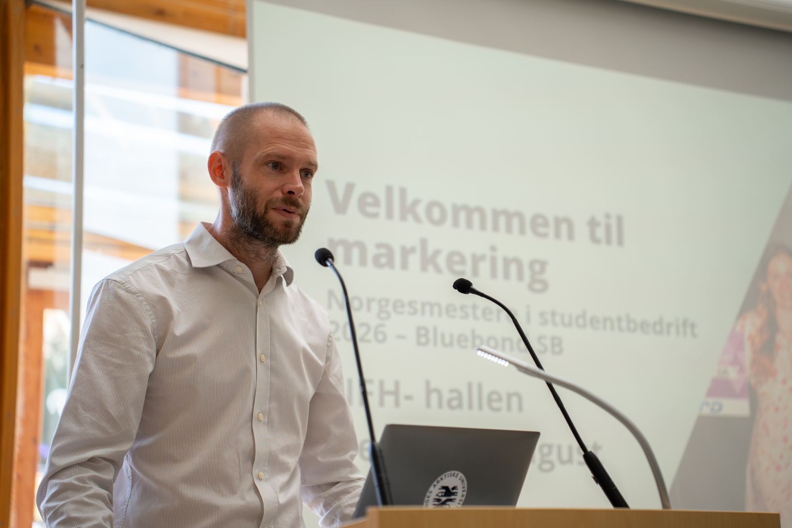 BlueBond SB-08781.jpg Mannlig dekan på talerstol i universitetsbygg.