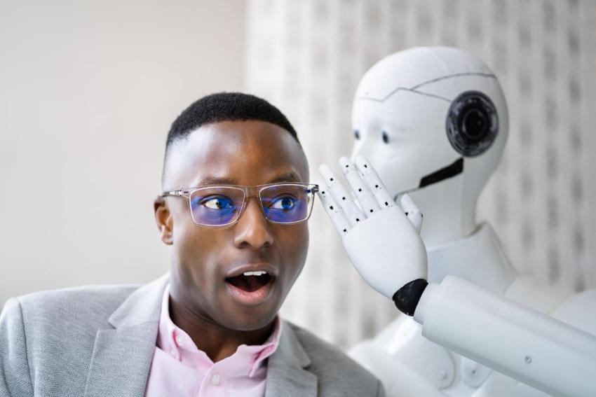 robot som visker noe i øret til en mann med mørk hudfarge og briller