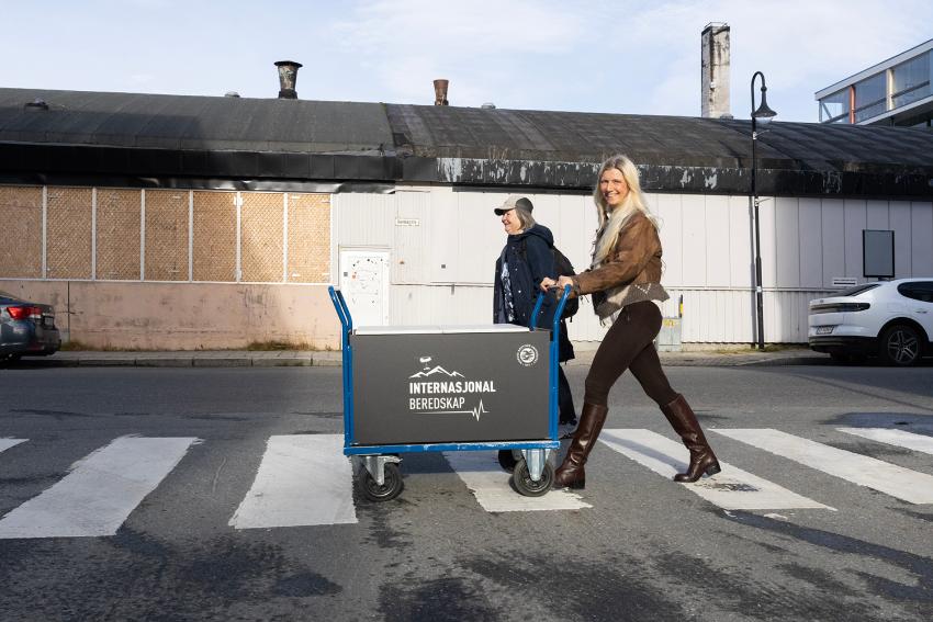 Kvinne krysser ei gate med ei stor tralle som inneholder blant annet kaffe og sjokolade.