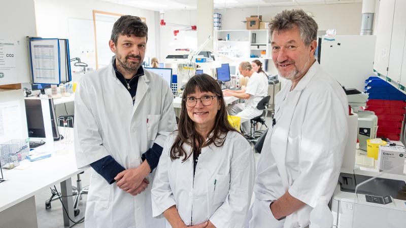 tre mennesker som st&aring;r sammen i laboratorium med hvite frakker p&aring;