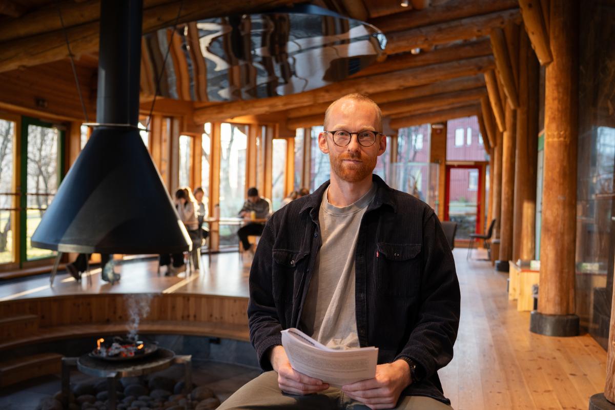Mann sitter foran b&aring;lplass i et samisk kulturhus med det dokument i hendene sine.