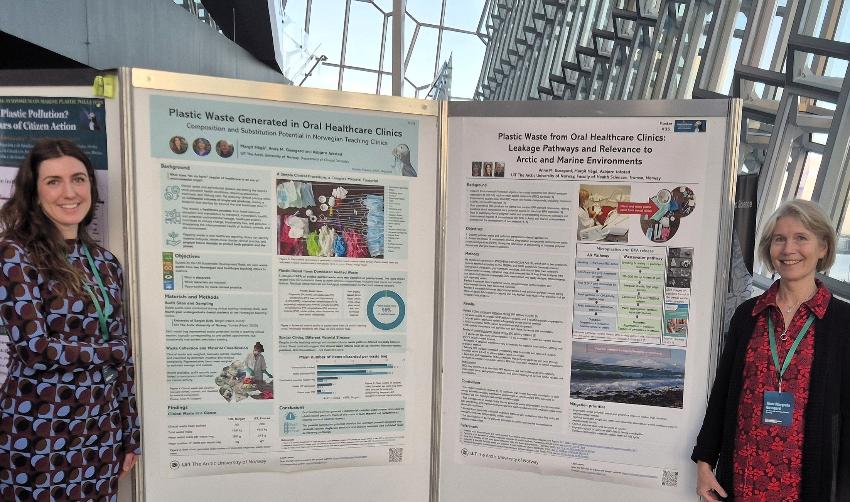 To kvinner står foran poster og smiler til kamera